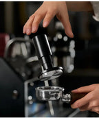 Black espresso tamper pressing into portafilter while hand holds basket below