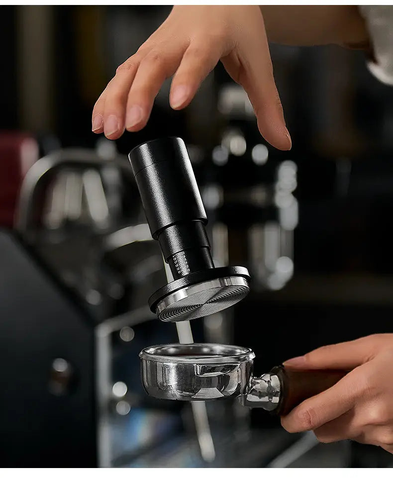 Black espresso tamper pressing into portafilter while hand holds basket below