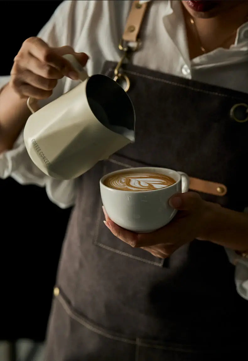 Milky white stainless milk pitcher pouring foamy latte art into a cup