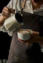 Milky white stainless milk pitcher pouring foamy latte art into a cup
