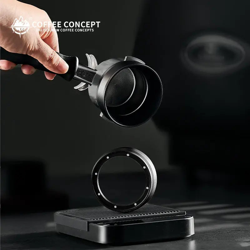 Black magnetic espresso dosing ring detached, held in hand above a round base plate.