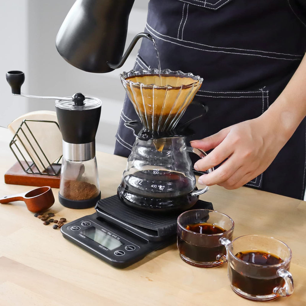 Hands pouring hot coffee into glass dripper on portable coffee maker kit with scale