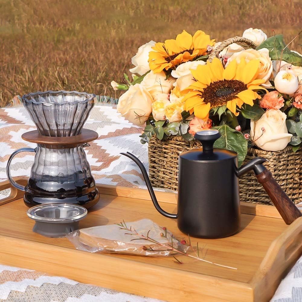 Outdoor pour-over coffee setup with glass dripper, gooseneck kettle, mug, and filter pack