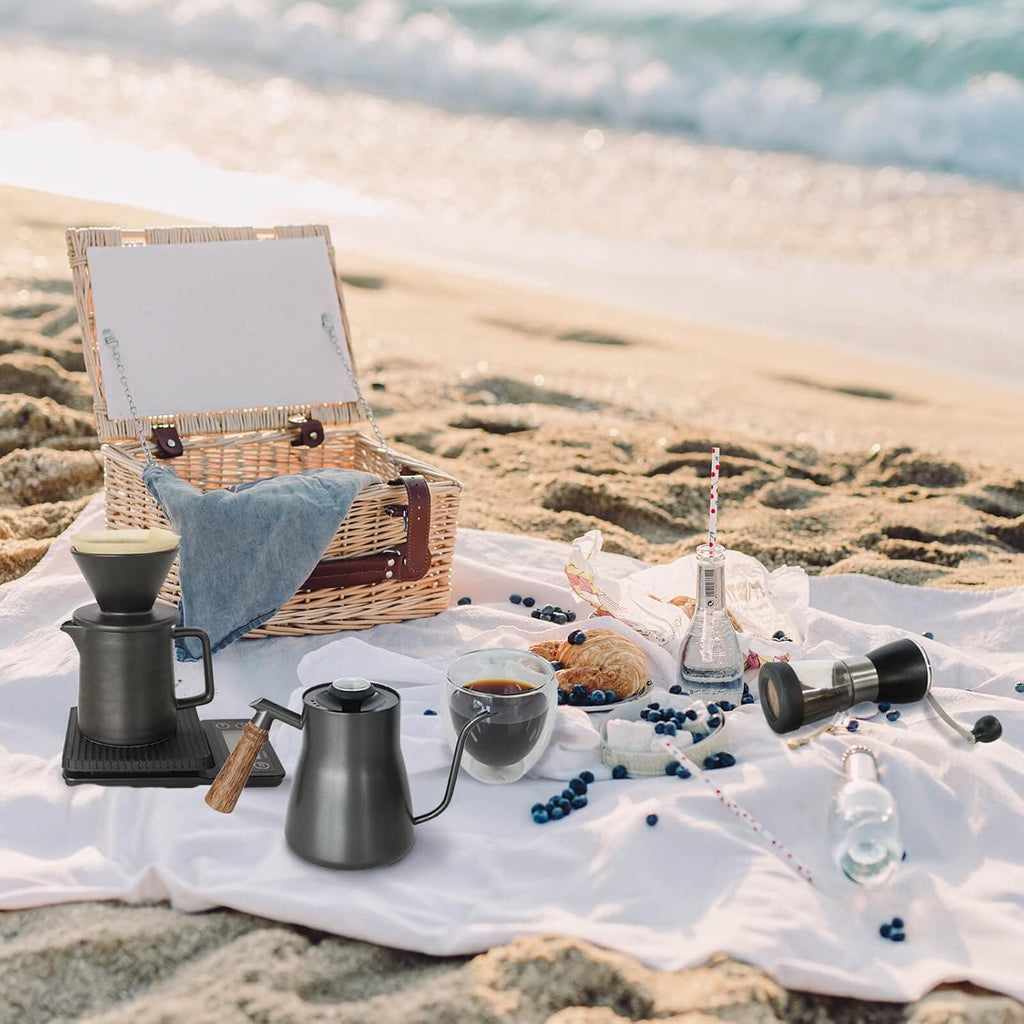 Outdoor portable pour-over coffee kit on picnic setup with kettle, dripper, mugs, grinder