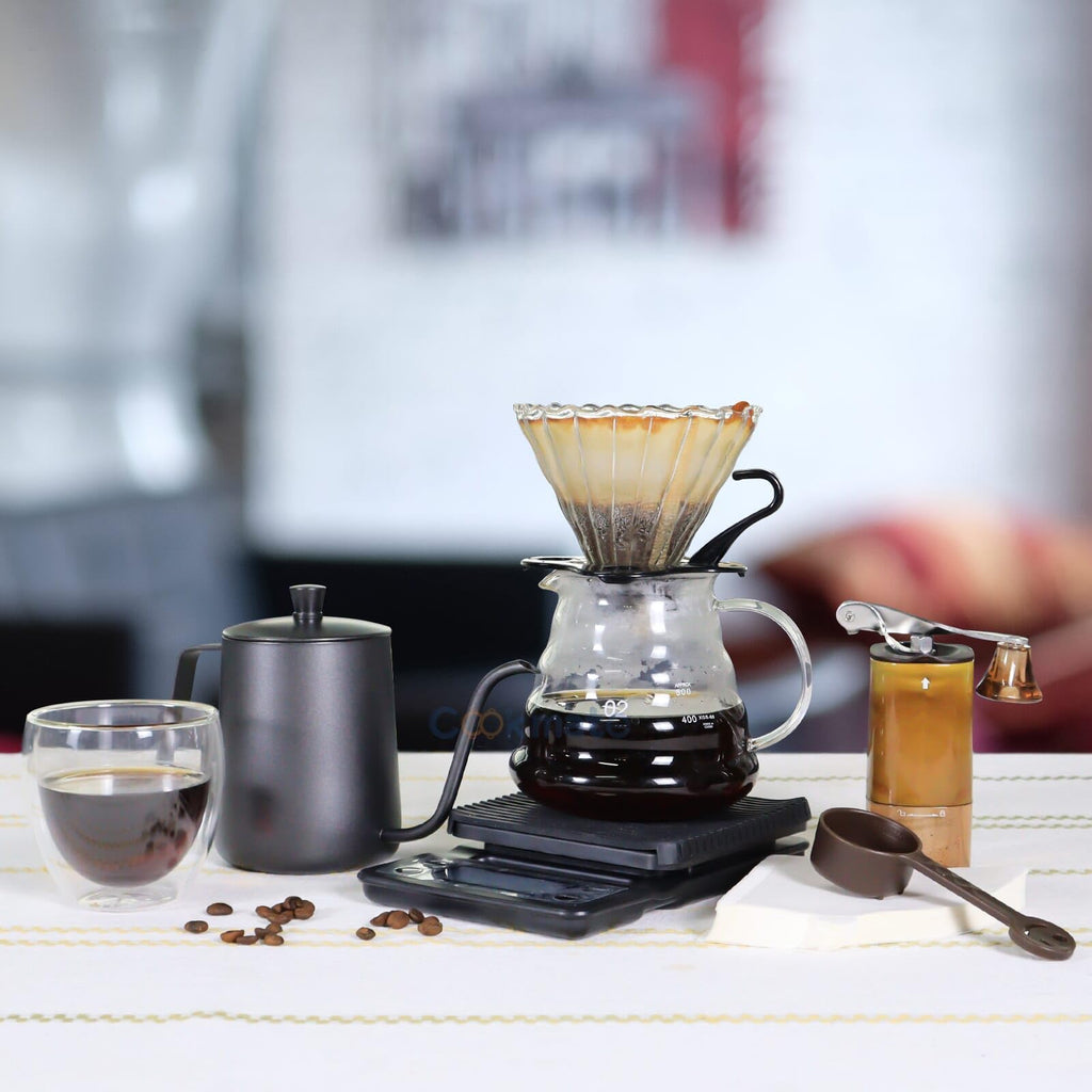 Pour-over coffee equipment set with glass dripper, dark kettle, grinder, and cups