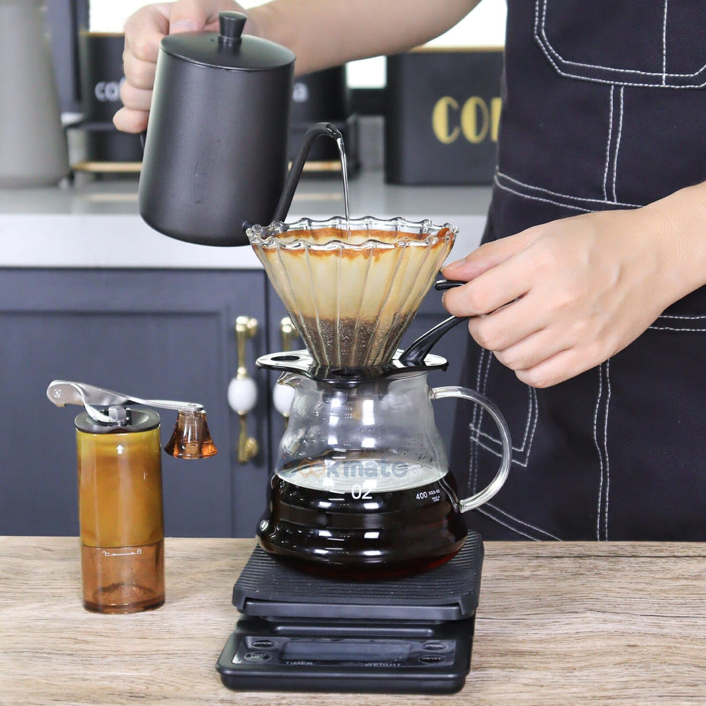 Pour-over coffee being brewed with glass dripper on brewer base and black carafe kettle