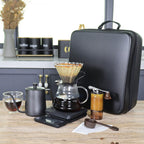 Countertop pour-over coffee brewer with glass carafe, kettle, and black zippered travel case