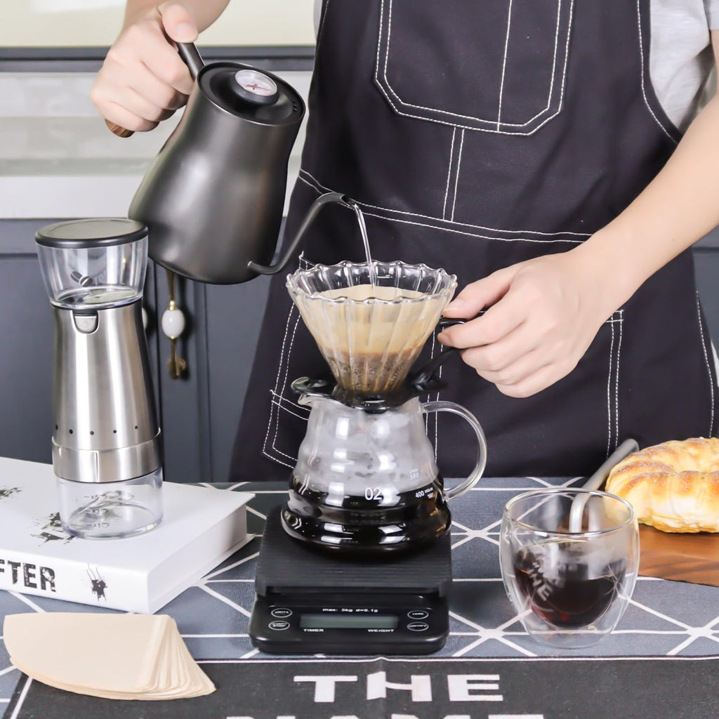 Pour-over coffee set on tabletop: stainless kettle, dripper, server cups, and black grinder base
