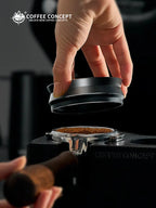 Black magnetic espresso dosing ring lifted by hand over a portafilter basket with grounds.