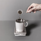Precision espresso and coffee scale holding a metal cup while grounds are poured