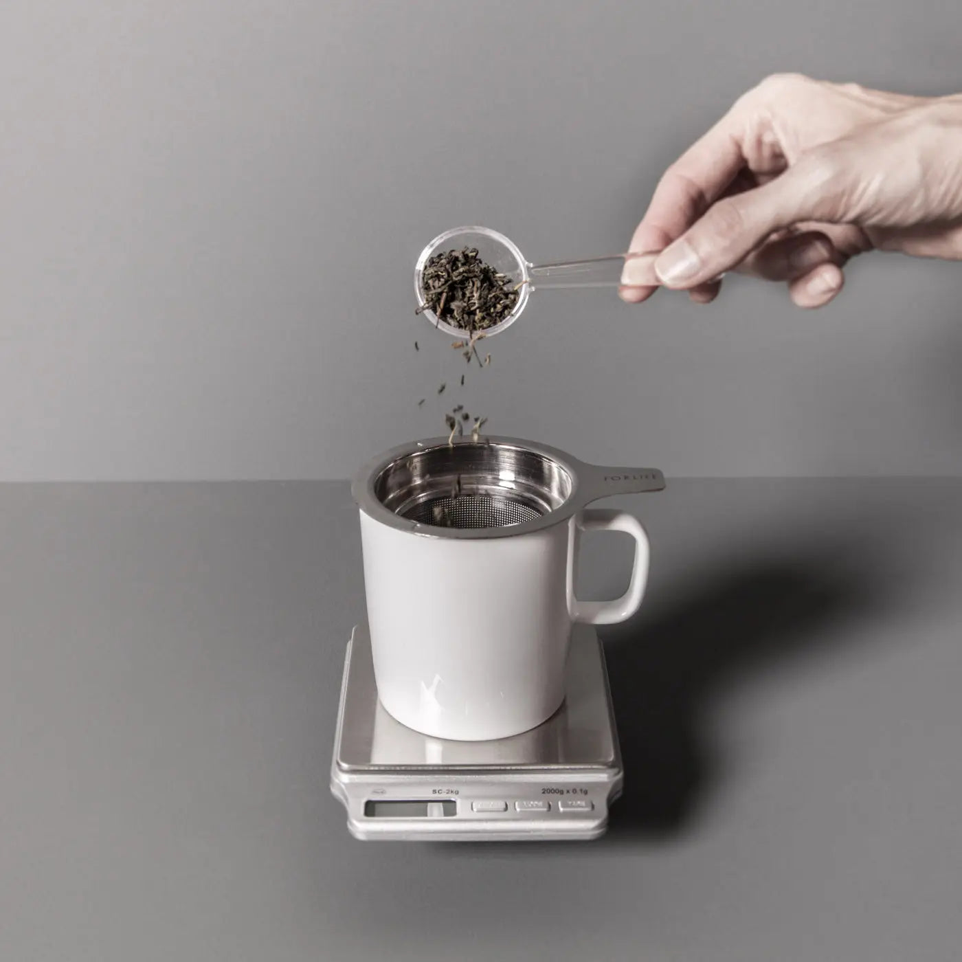 Precision espresso and coffee scale holding a metal cup while grounds are poured