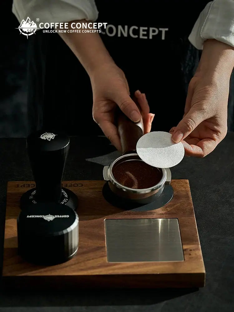Hands placing a white coffee filter paper disc onto a portafilter basket