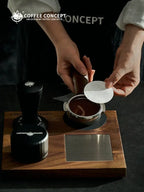 Hands placing a white coffee filter paper disc onto a portafilter basket