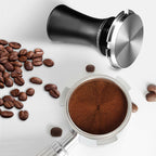 Top view of spring-loaded espresso tamper with stainless disc and espresso grounds
