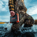 Rugged XL power bank in orange and black, held in hand near water