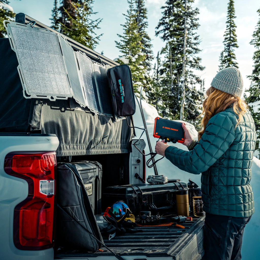 Orange-and-black rugged XL power bank mounted in a vehicle trunk, person charging